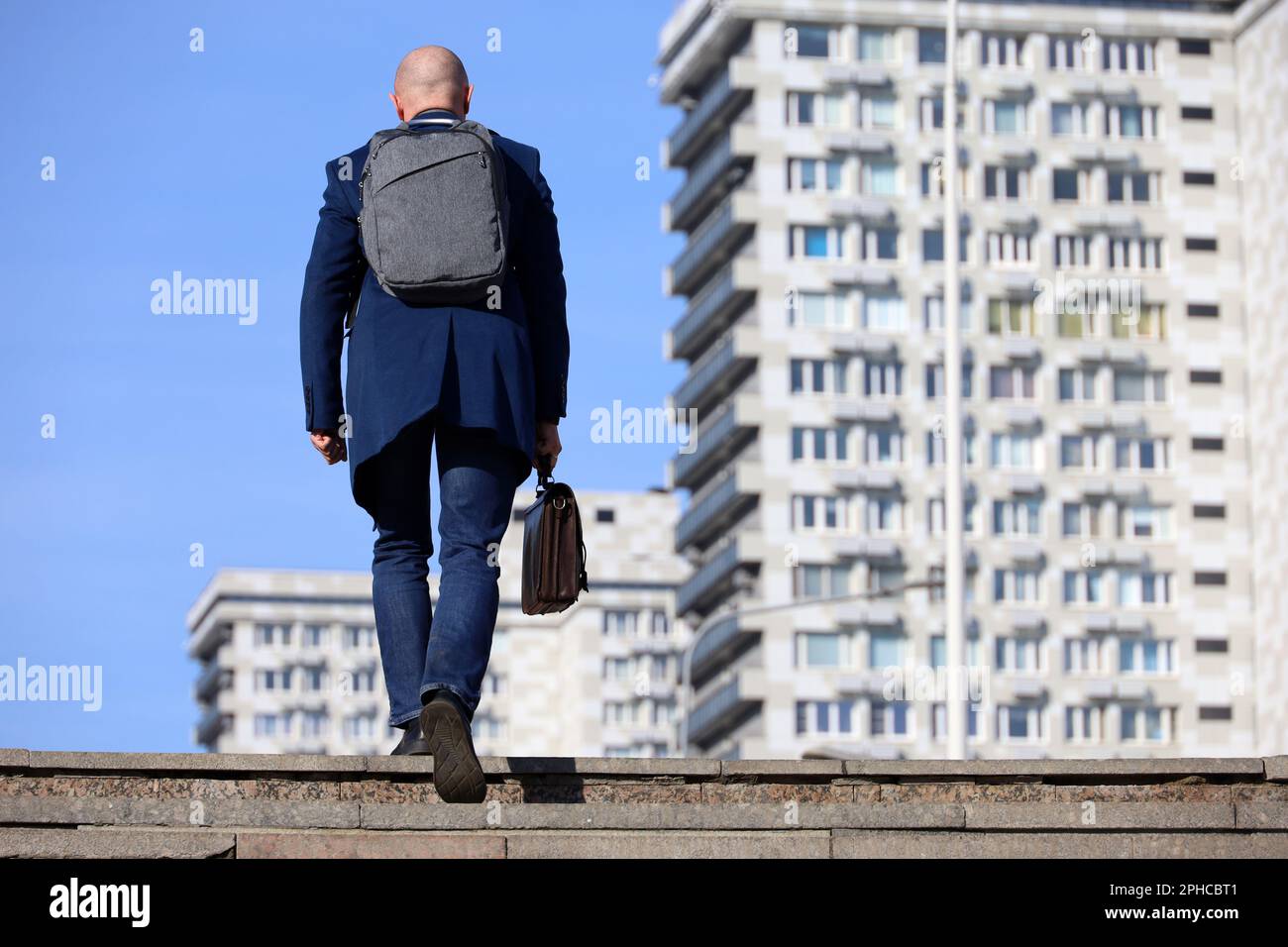 Uomo d'affari con zaino e valigetta in pelle in mano scalando scale in pietra in città. Concetto di carriera, di successo, di spostamento verso l'alto Foto Stock