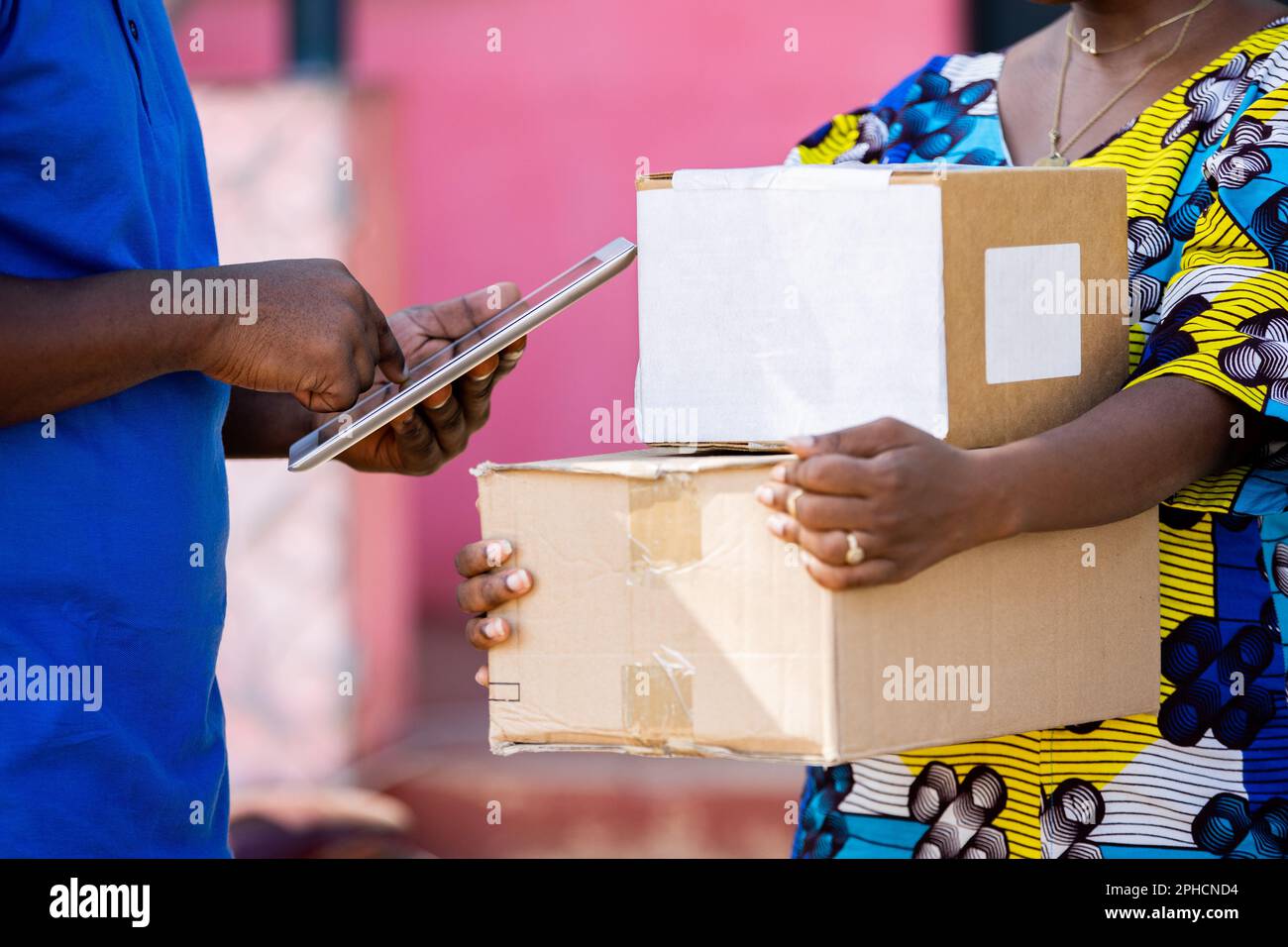 African Postal Delivery Man registra i dettagli di ricezione della confezione di cartone spedita con un tablet digitale intelligente acquistato online da una cliente femminile. Foto Stock
