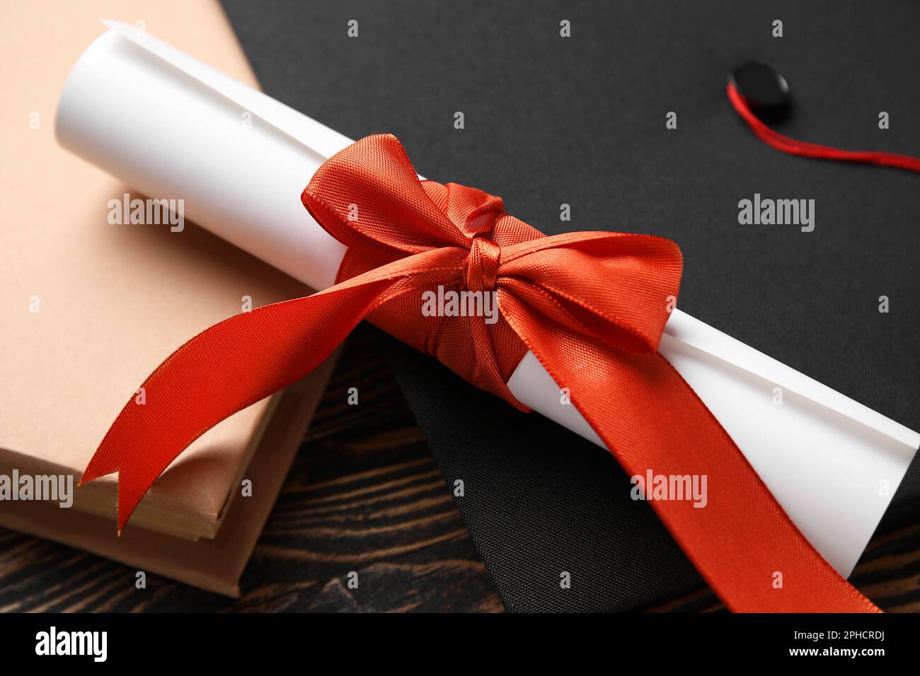 Diploma con nastro rosso, cappello di laurea e libro su tavolo di legno Foto Stock