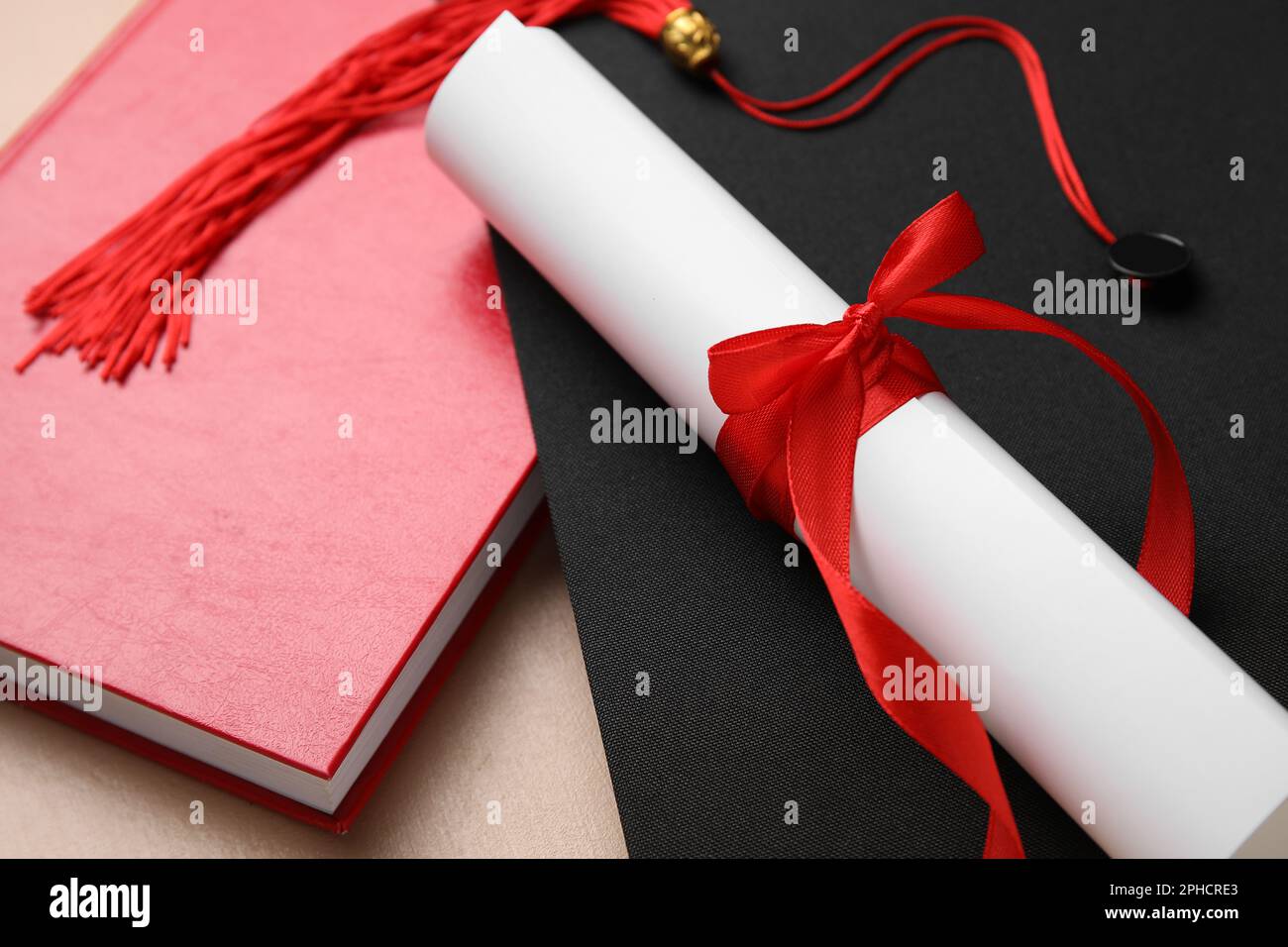 Diploma con nastro rosso, cappello di laurea e libro su tavolo beige Foto Stock