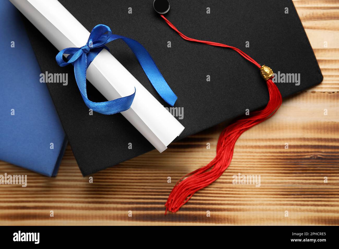 Diploma con nastro blu, cappello di laurea e libro su tavolo di legno Foto Stock