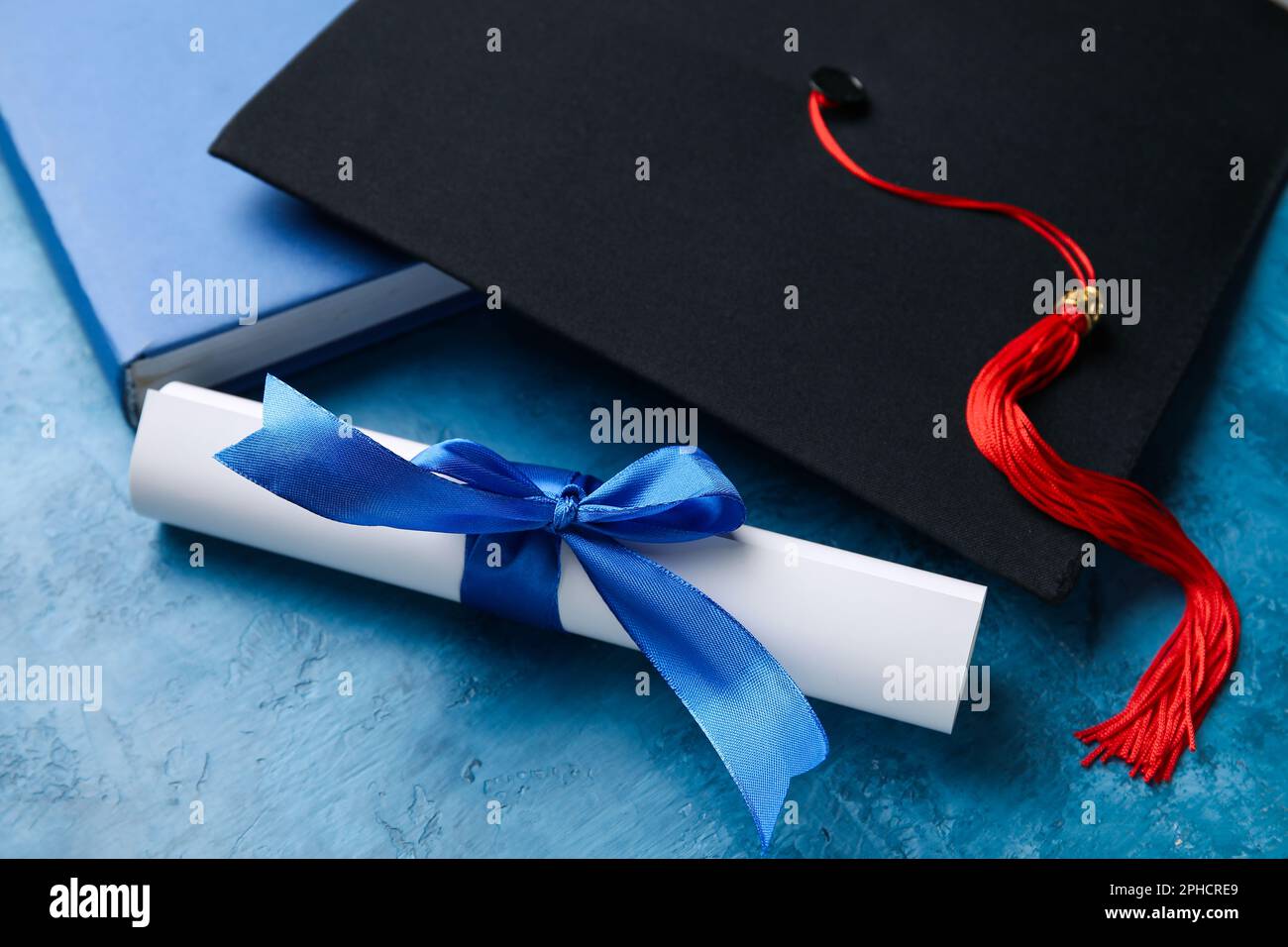 Diploma con nastro, cappello di laurea e libro su tavolo blu Foto Stock