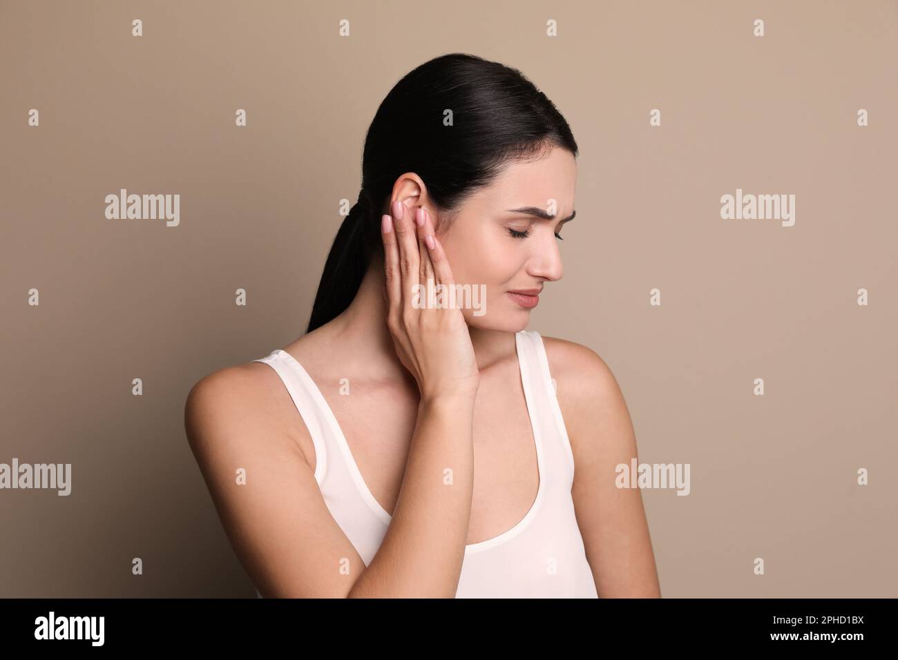 Giovane donna che soffre di dolore all'orecchio su sfondo grigio Foto Stock