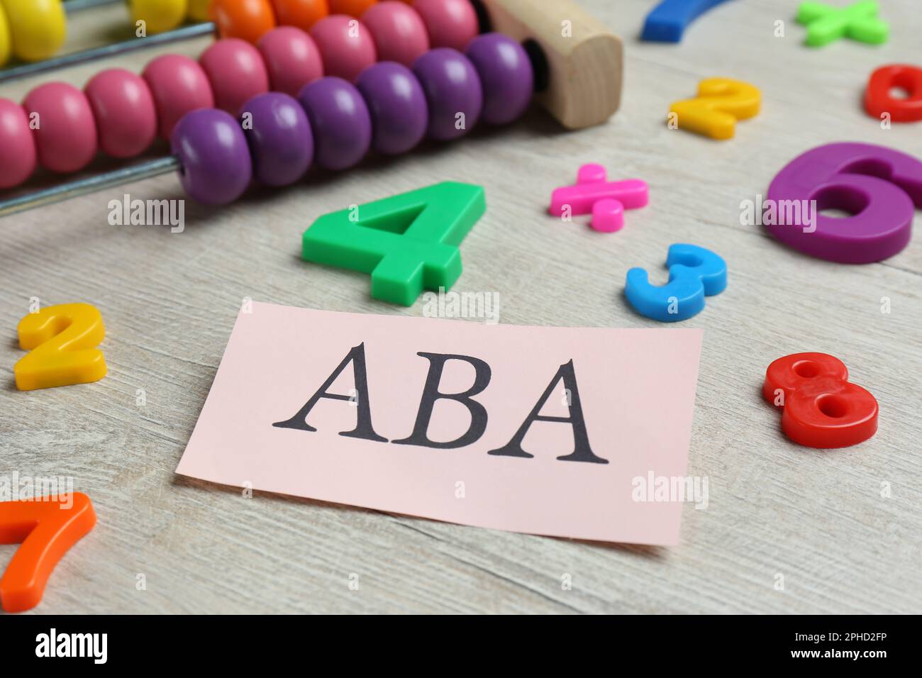 Foglio di carta con abbreviazione ABA (Applied Behavior Analysis), abaco e numeri colorati su tavola di legno bianco, primo piano Foto Stock