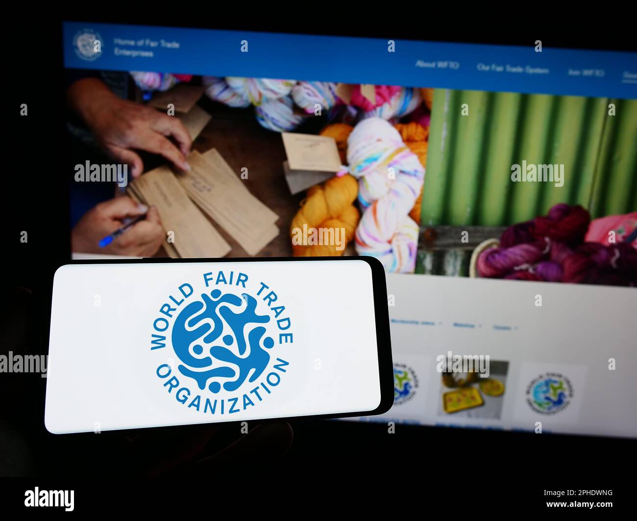 Persona che tiene in mano uno smartphone con il logo della World Fair Trade Organization (WFTO) sullo schermo di fronte al sito Web. Messa a fuoco sul display del telefono. Foto Stock