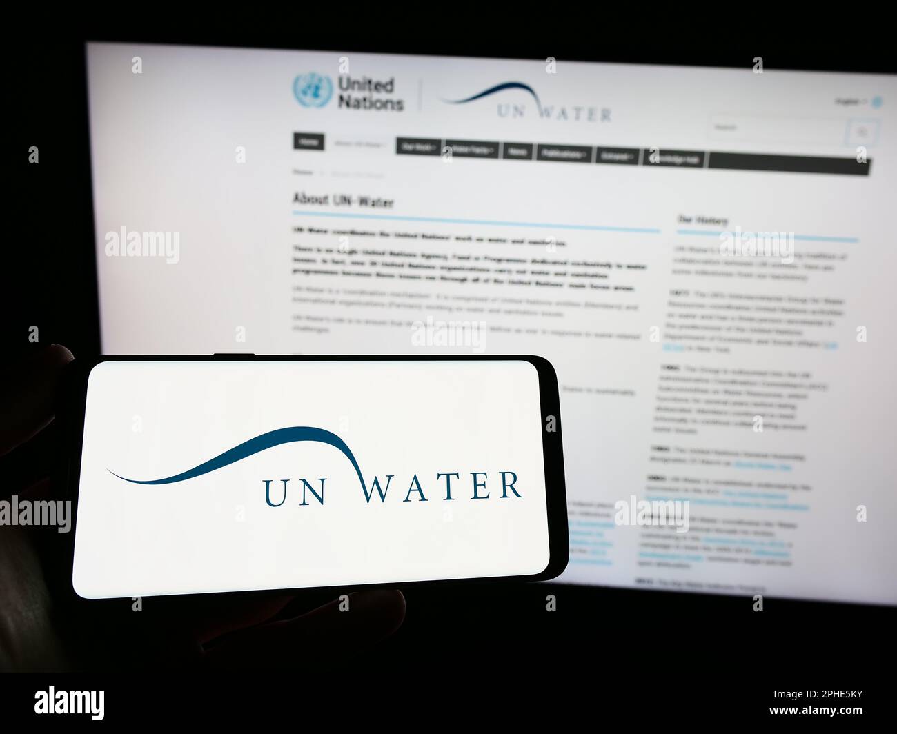 Persona in possesso di smartphone con il logo dell'agenzia delle Nazioni Unite acqua (un-acqua) sullo schermo di fronte al sito web. Messa a fuoco sul display del telefono. Foto Stock