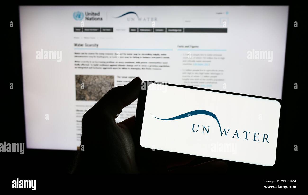 Persona che tiene il telefono cellulare con il logo dell'agenzia delle Nazioni Unite acqua (un-acqua) sullo schermo di fronte alla pagina web. Messa a fuoco sul display del telefono. Foto Stock