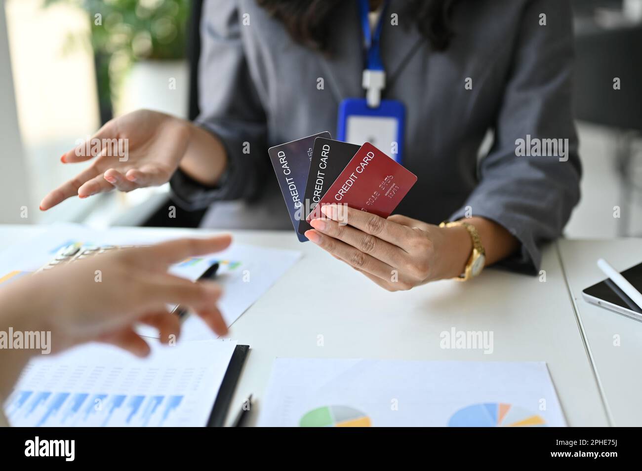 Immagine ritagliata di un banchiere femminile asiatico professionale che mostra vari tipi di carte di credito a un cliente durante la riunione presso la banca. Foto Stock