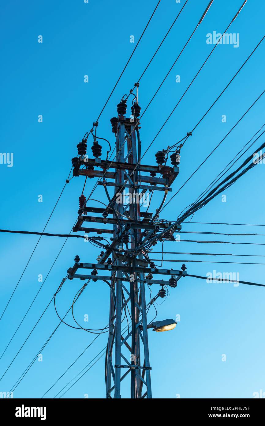 Vecchia rete elettrica e palo della luce stradale con cavi e fili contro il cielo blu di sera Foto Stock