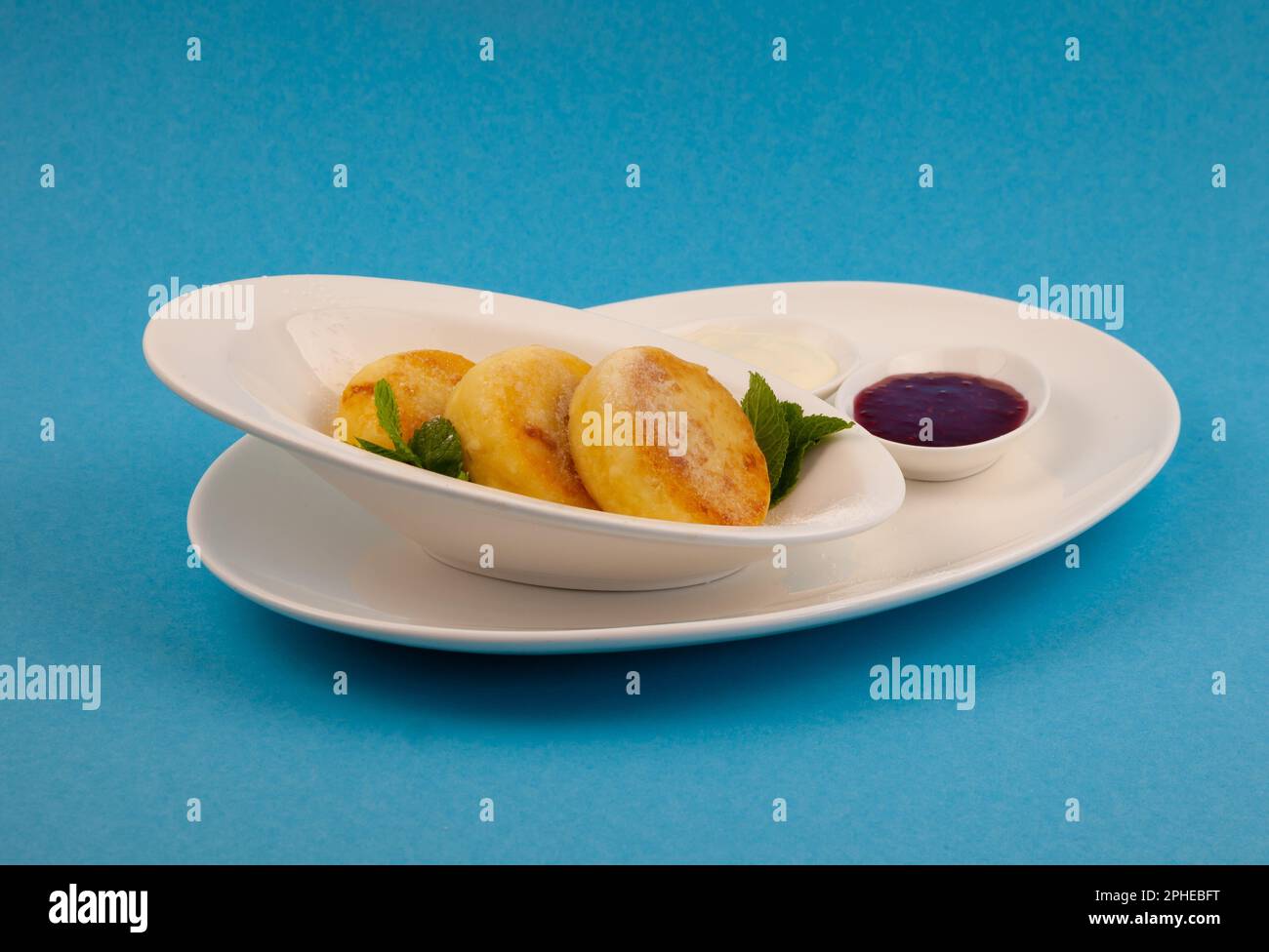 Frittelle di formaggio ricotta rotonda in un piatto bianco su sfondo blu. Cibo prima colazione. Cibo sano. Salsa di panna acida e menta. Primo piano vista dall'alto. Pasto dessert. Frittelle di ricotta al formaggio ricotta. Foto Stock
