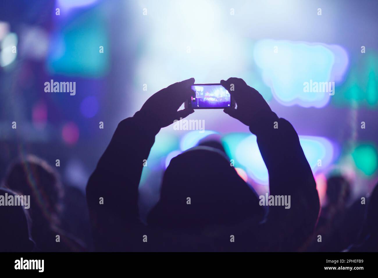 Profilo della vista posteriore di una persona irriconoscibile che prende video con lo smartphone mentre guardi lo spettacolo moderno contro il palcoscenico illuminato al neon Foto Stock