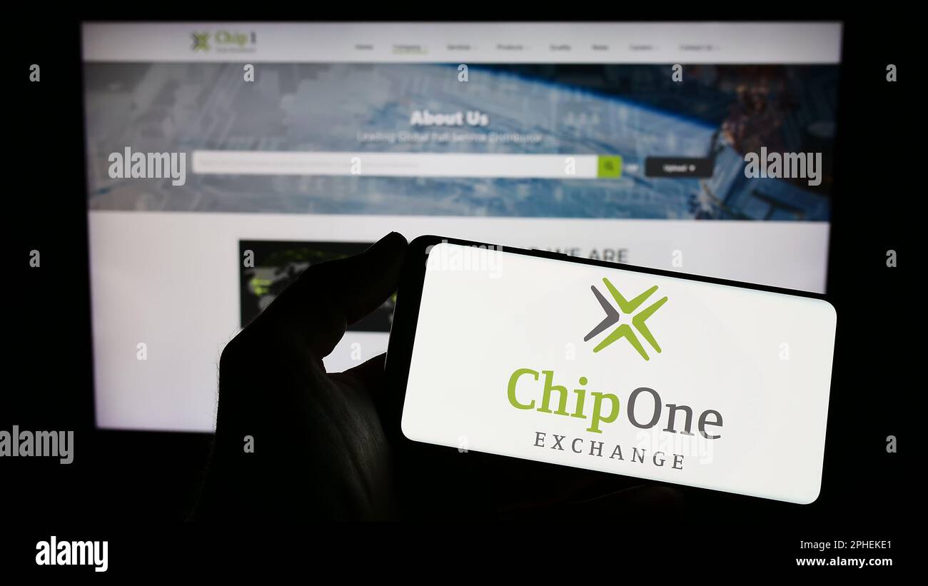 Persona che tiene il telefono cellulare con il logo della società di distribuzione tedesca chip 1 Exchange sullo schermo di fronte alla pagina web. Messa a fuoco sul display del telefono. Foto Stock