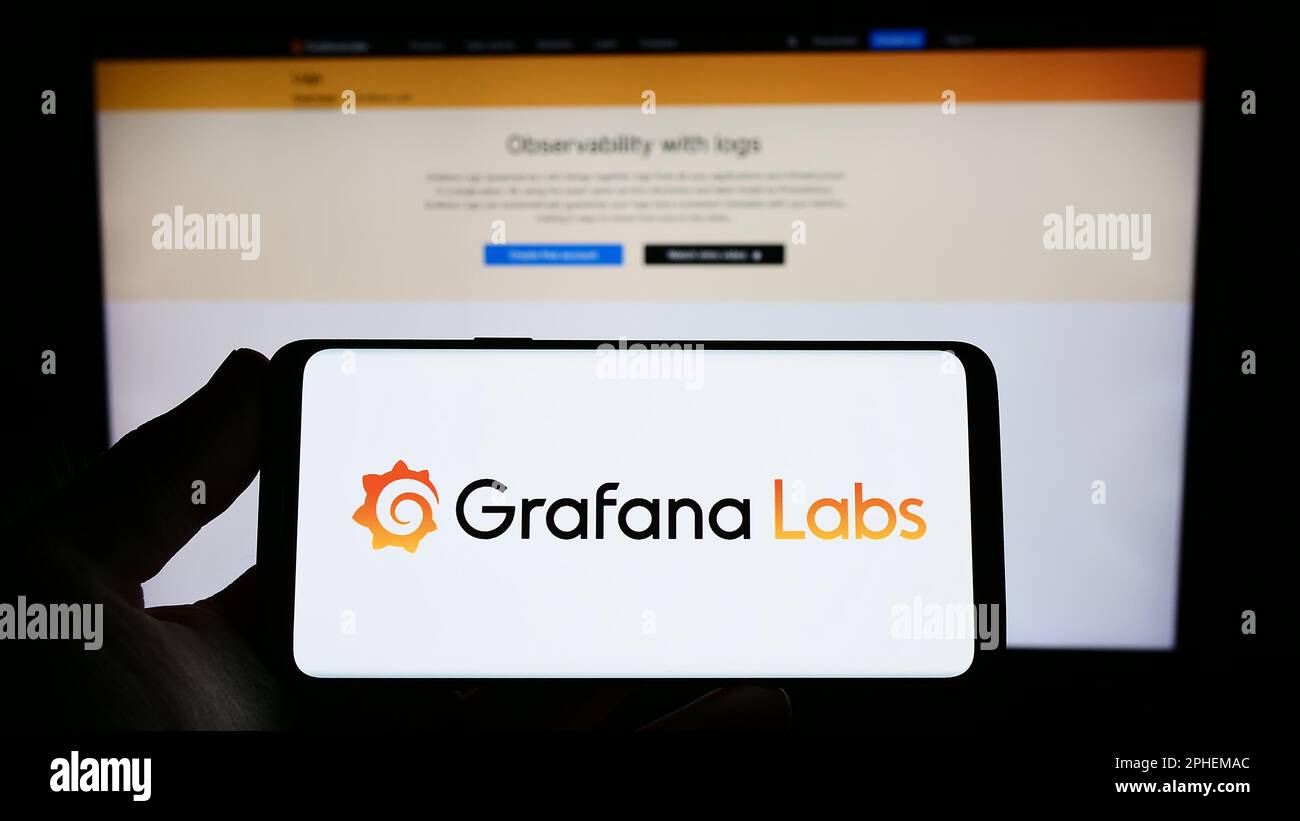 Persona che tiene uno smartphone con il logo della società di software di analisi degli Stati Uniti Grafana Labs sullo schermo di fronte al sito Web. Messa a fuoco sul display del telefono. Foto Stock