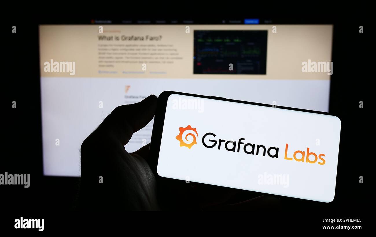 Persona che tiene il telefono cellulare con il logo della società americana di software di analisi Grafana Labs sullo schermo di fronte alla pagina web. Messa a fuoco sul display del telefono. Foto Stock