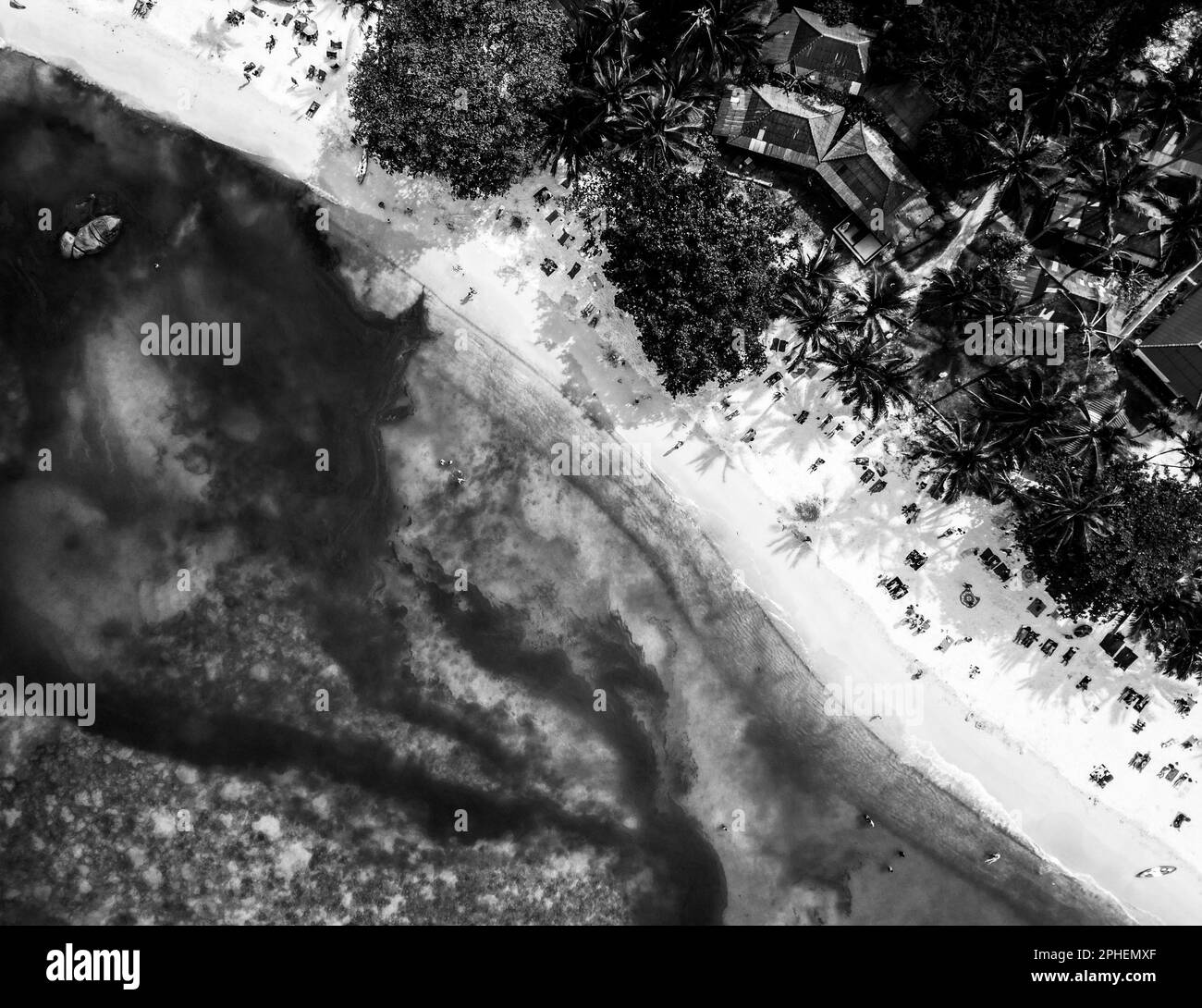 Una scala di grigi aerea di edifici rustici sulla riva separati da acque marine, perfetto per sfondi Foto Stock