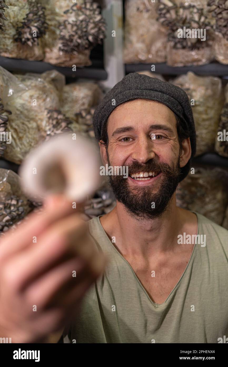 Giovane uomo felice tenendo funghi ostriche contro la serra dei funghi. Foto Stock