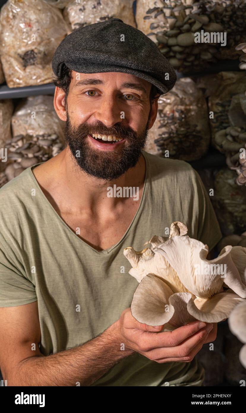 Giovane uomo felice tenendo funghi ostriche contro la serra dei funghi. Foto Stock