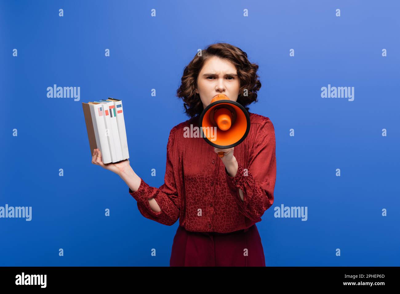 un insegnante di lingua rigoroso che tiene libri di testo e urla in megaphone isolato su blu, immagine di scorta Foto Stock
