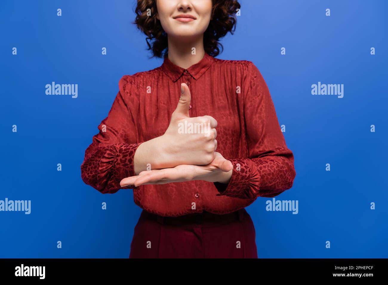 vista parziale della donna positiva in borgogna blusa mostrando gesto che significa aiuto sul linguaggio dei segni isolato su blu, immagine stock Foto Stock