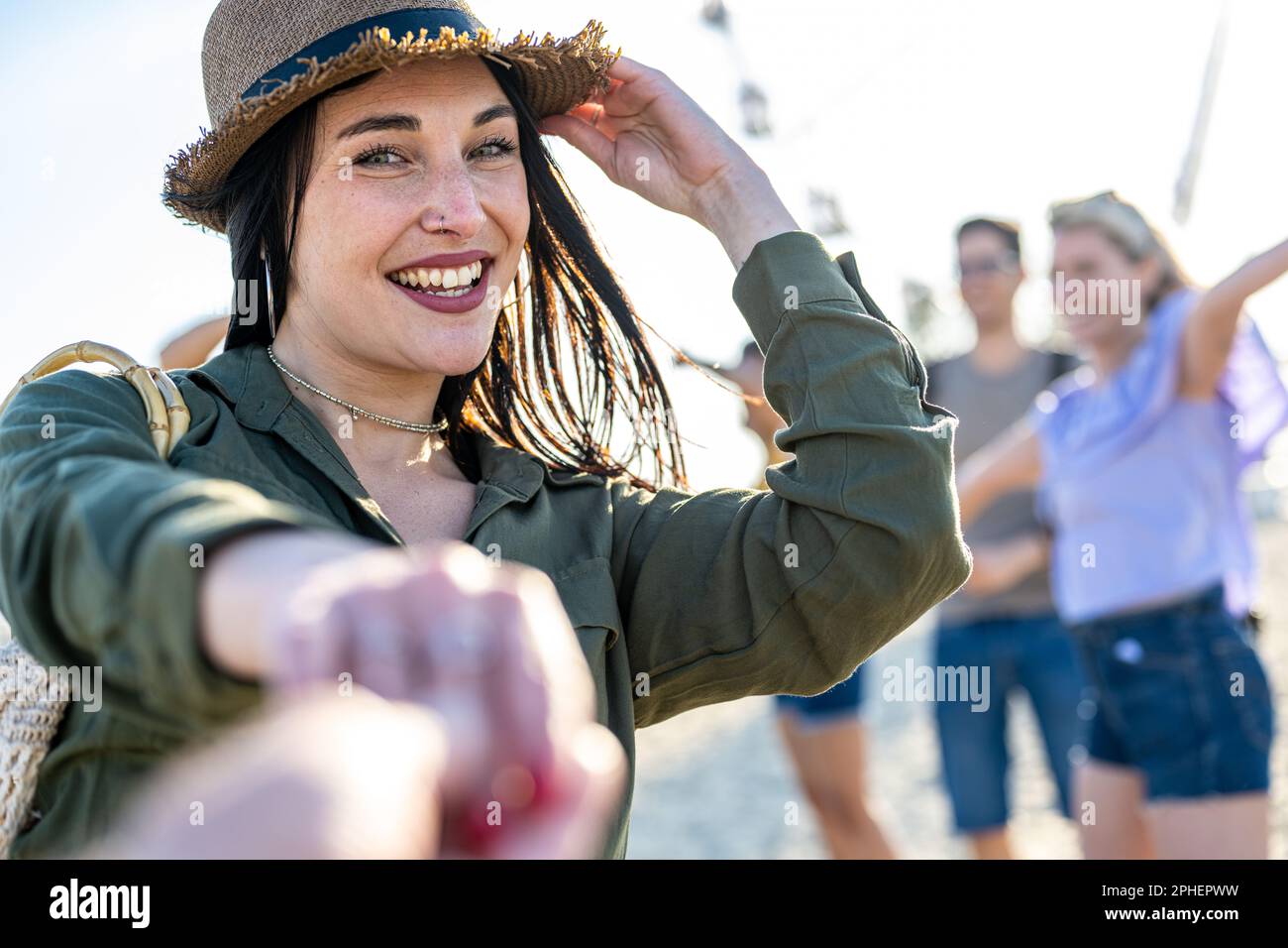 Giovane bruna donna con occhi blu che invita a ballare in una festa sulla spiaggia, festival musicale internazionale con una folla felice di persone Foto Stock