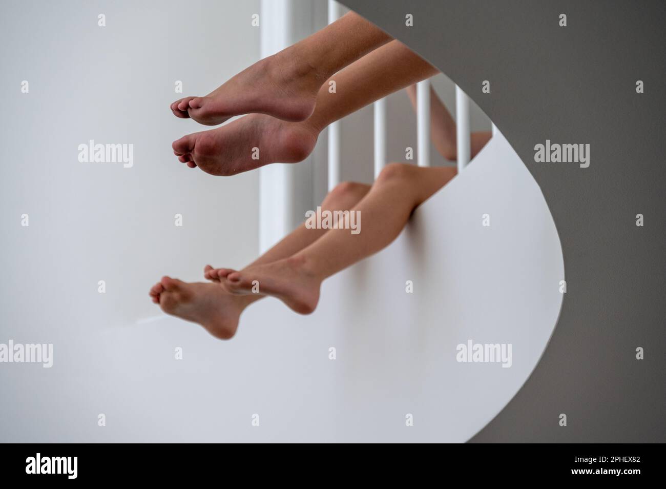 Le gambe dei bambini pendono sul bordo di un balcone interno. Foto Stock