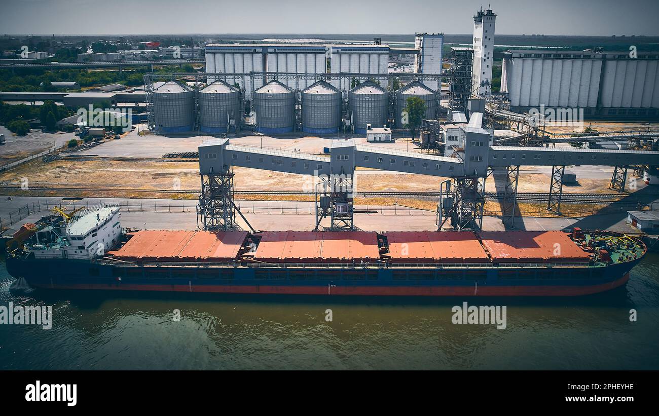 Nave portarinfuse nel porto di carico. Vista aerea della chiatta in un molo. Elevatore di grano e sili granari sullo sfondo. Foto Stock
