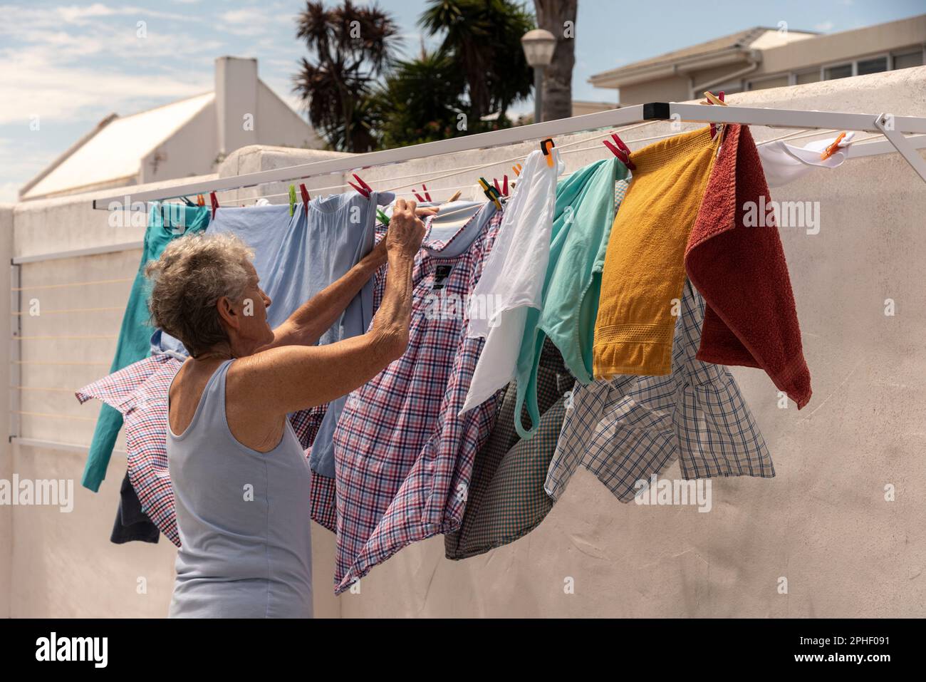 Langebaan, Sudafrica. 2023. Donna anziana che appende il lavaggio in una giornata ventosa nel suo cortile. Foto Stock