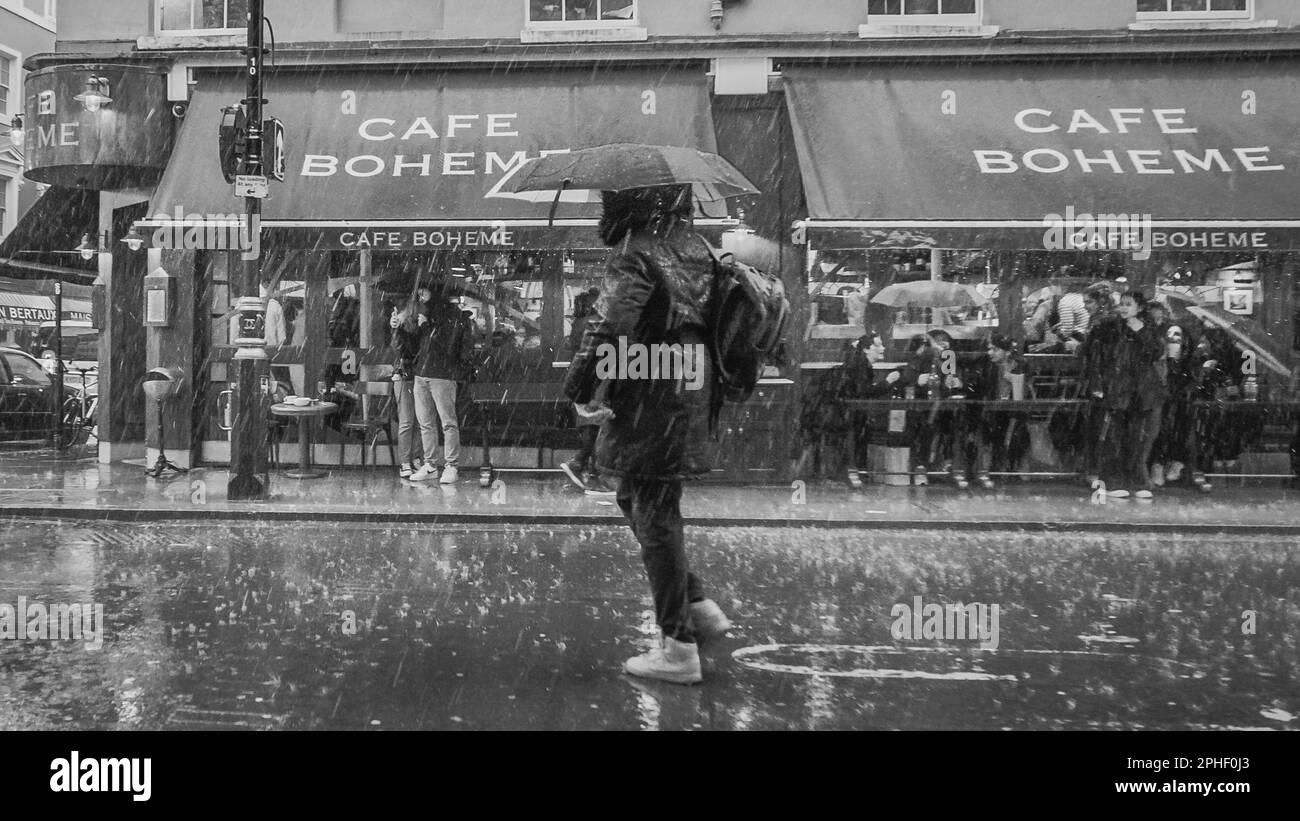 Immagine in bianco e nero di un pedone catturato dalla forte pioggia del Soho di Londra. Foto Stock