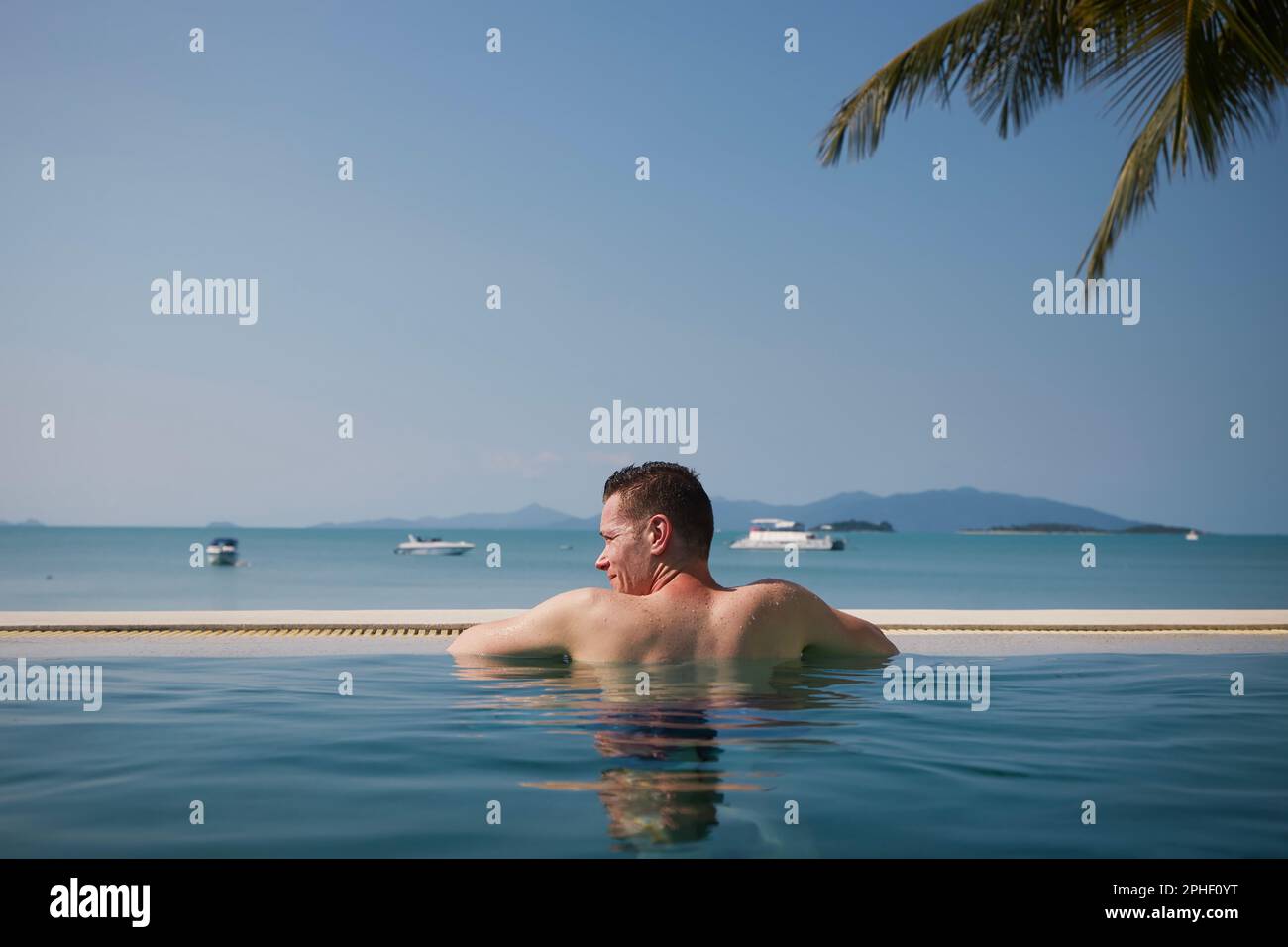 Vista posteriore uomo mentre si rilassa in piscina contro il mare con isole. Vacanza sulla spiaggia in una destinazione tropicale. Foto Stock