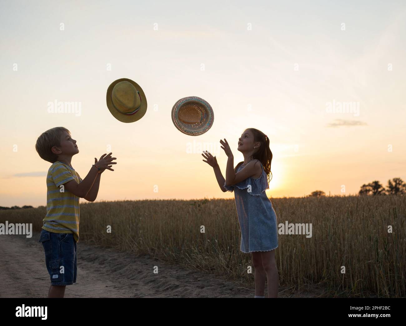 silhouette di una ragazza e di un ragazzo di 6 anni, lancia e cattura cappelli sullo sfondo del tramonto. Famiglia, amicizia, prole, infanzia gioiosa, h Foto Stock