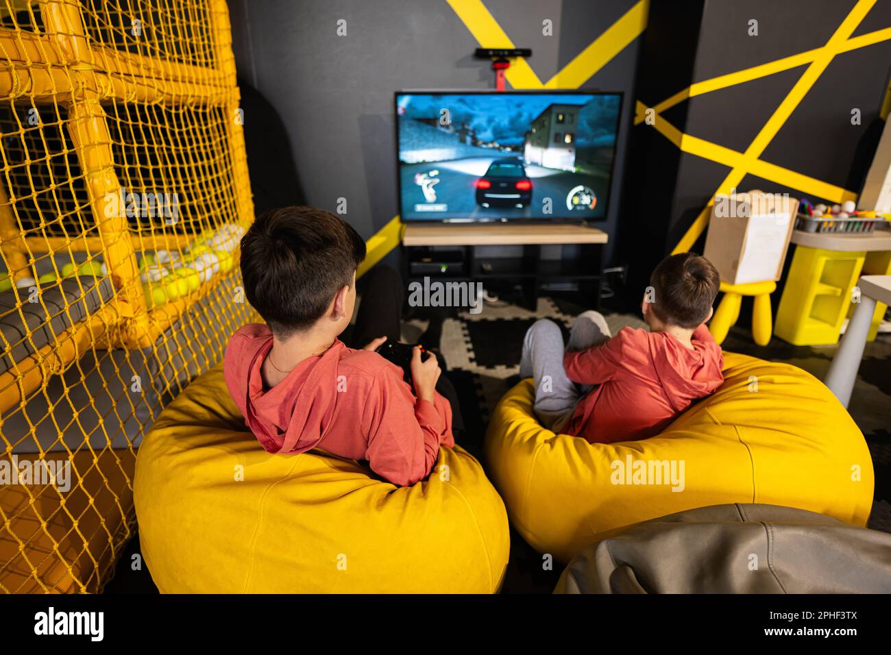 Due fratelli che giocano a una console di gioco per le corse, seduti sul  pouf giallo nel centro giochi per bambini Foto stock - Alamy