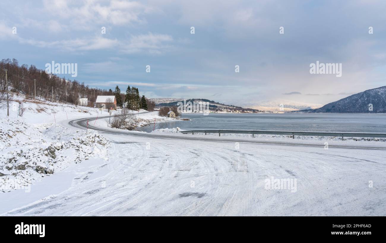 Vista panoramica sui fiordi e sulle ripide montagne innevate da Senja, Norvegia. Barca, pesci secchi, cespugli innevati e betulle sulla spiaggia. inverno Foto Stock