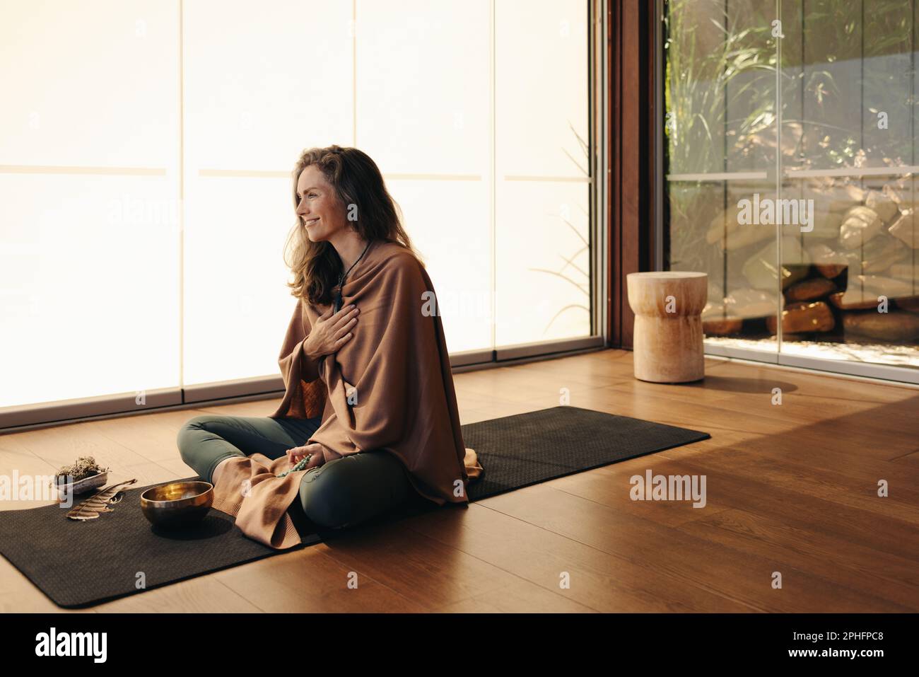 Donna anziana felice meditando usando la medicina alternativa nel paese. Donna matura che pratica una cerimonia auto-guaritrice e purificante su un tappetino yoga. Cheerfu Foto Stock