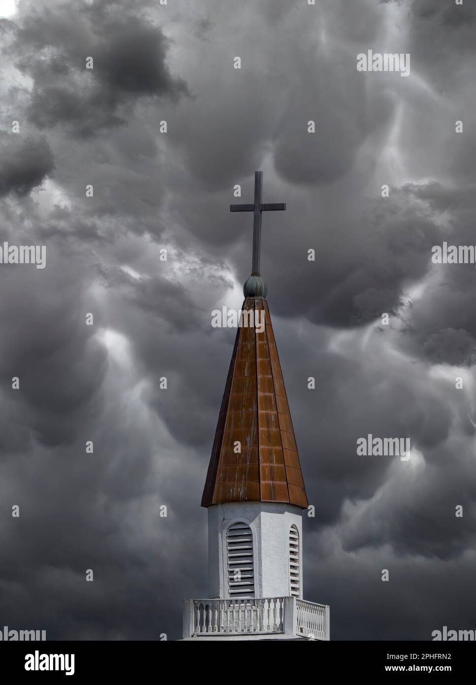 Campanile della chiesa con croce in cima contro un cielo scuro tempestoso Foto Stock