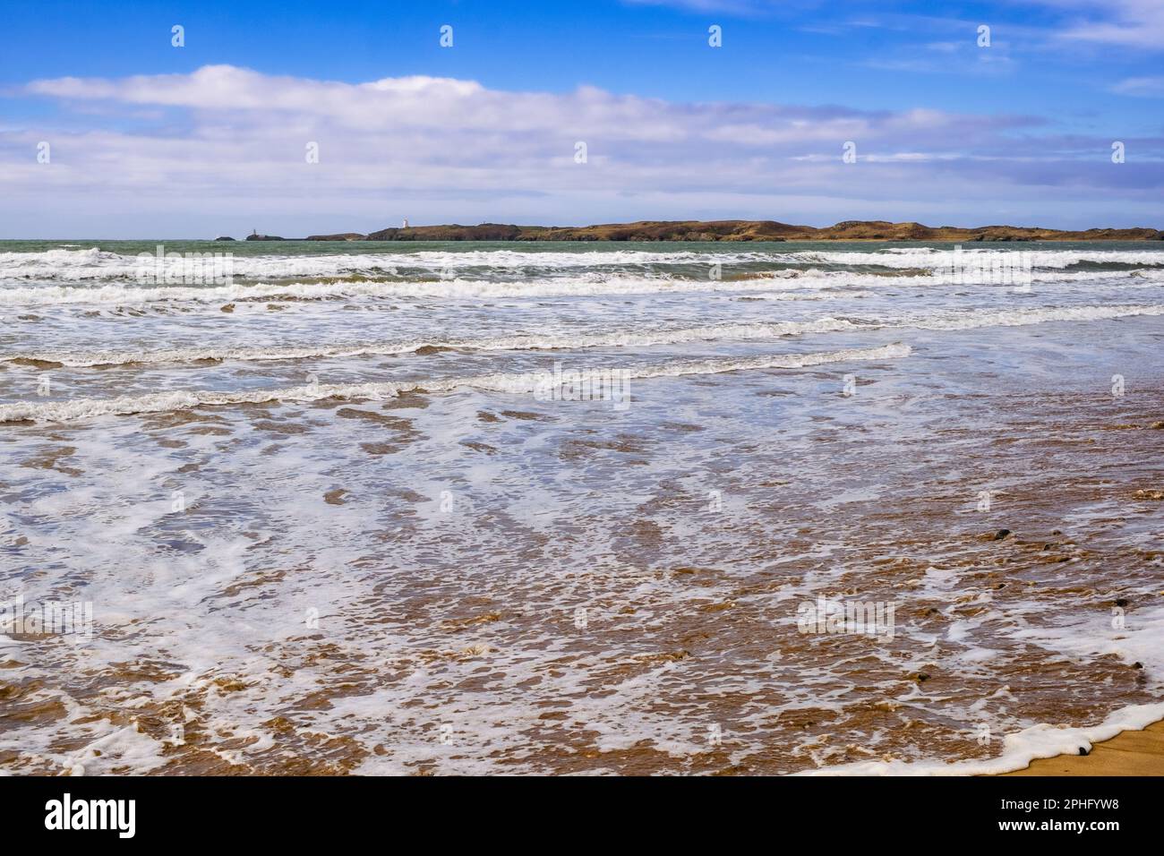 Le onde si dirigono verso la spiaggia sabbiosa di Newborough, con l'alta marea che guarda verso l'isola di Llanddwyn. Newborough, Isola di Anglesey, Galles, Regno Unito, Gran Bretagna, Europa Foto Stock