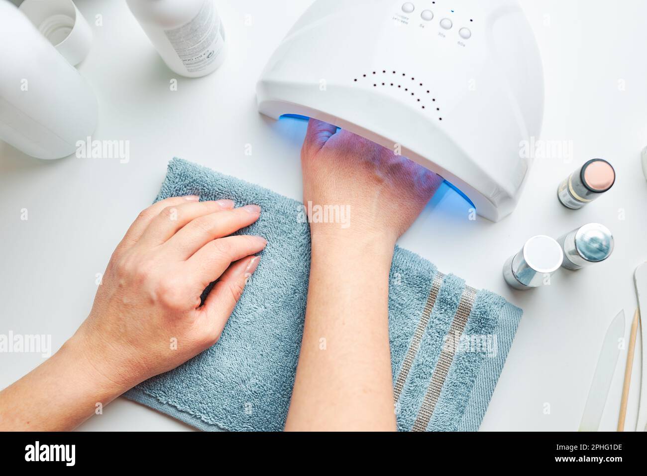 Donna che applica gel ibrido lucidare utilizzando lampada UV. Concetto di trattamento spa beauty wellness. Prodotti cosmetici, lampada UV, foglie verdi su tavola bianca. Centro benessere, m Foto Stock