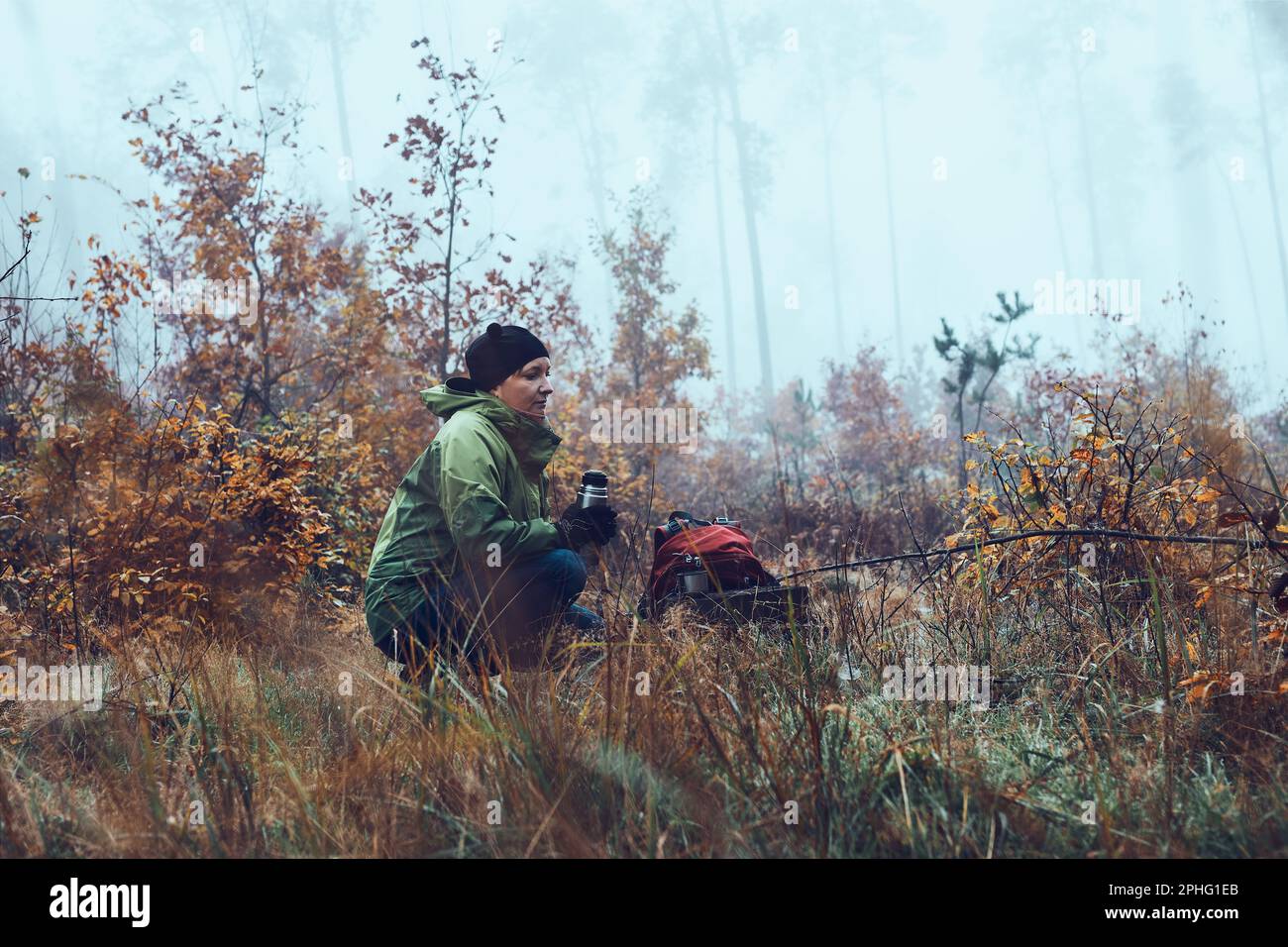 Donna con zaino in pausa durante il viaggio autunnale bere una bevanda calda da thermos beuta il giorno freddo autunnale. Attiva donna di mezza età che vagare arou Foto Stock