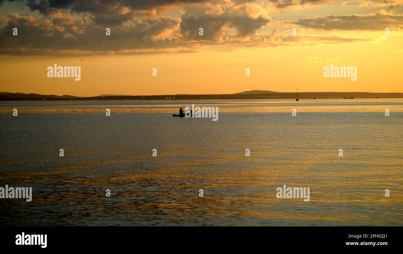 Nuvolosità sul lago al tramonto con silhouette di coppia in tavola da surf Foto Stock