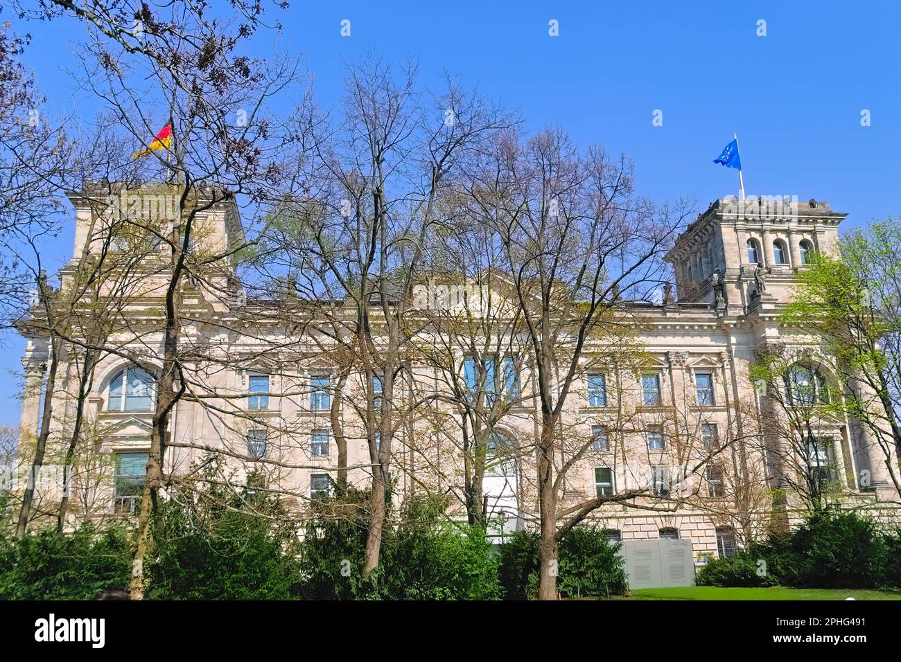 Parco vicino al Reichstag a Berlino. Dietro gli alberi si trovano le cupole del Bundestag e le bandiere della Germania e dell'Unione europea. Foto Stock