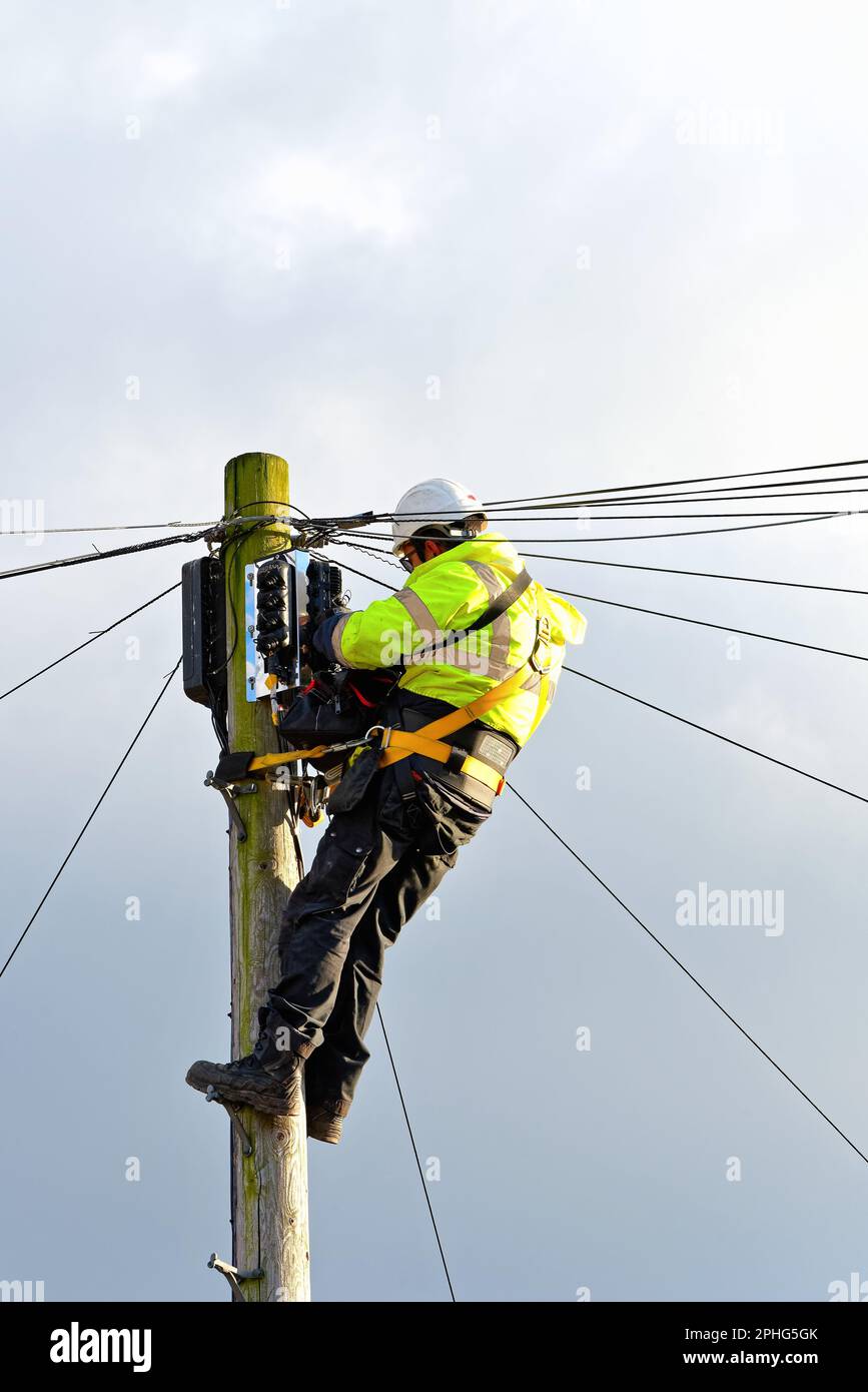 Un ingegnere di British Telecoms che installa il cavo a fibra ottica alla parte superiore di un palo telefonico Inghilterra Regno Unito Foto Stock