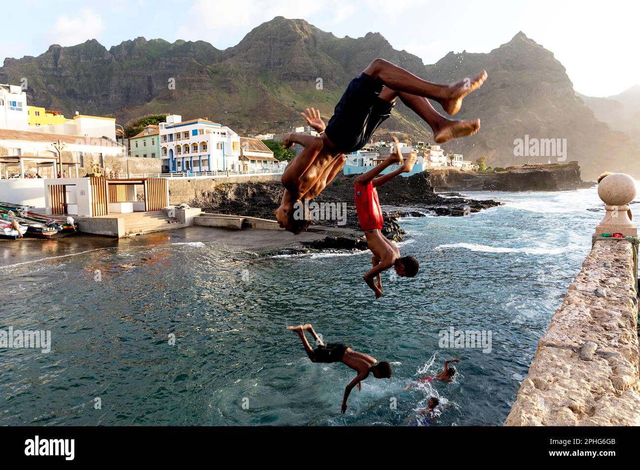 Ragazzi locali che saltano dal molo al mare nel porto di Ponta do Sol con spettacolari montagne sullo sfondo, Santo Antao, Cabo verde Foto Stock