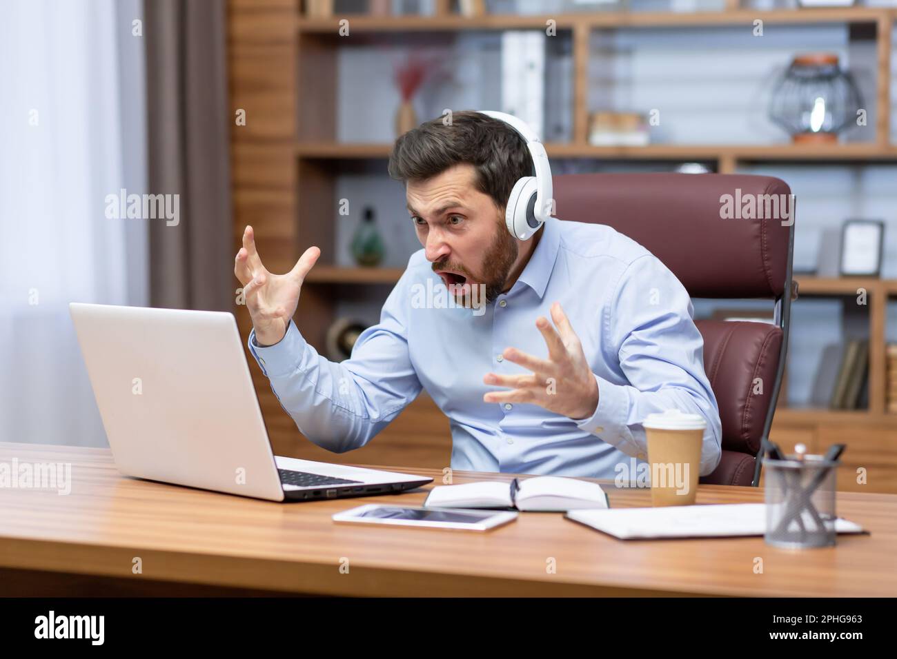 Un uomo d'affari arrabbiato ha deluso la visione di una partita sportiva sul posto di lavoro, il capo in una camicia che allietava l'ufficio, un uomo anziano maturo in cuffie che grida allo schermo del notebook. Foto Stock