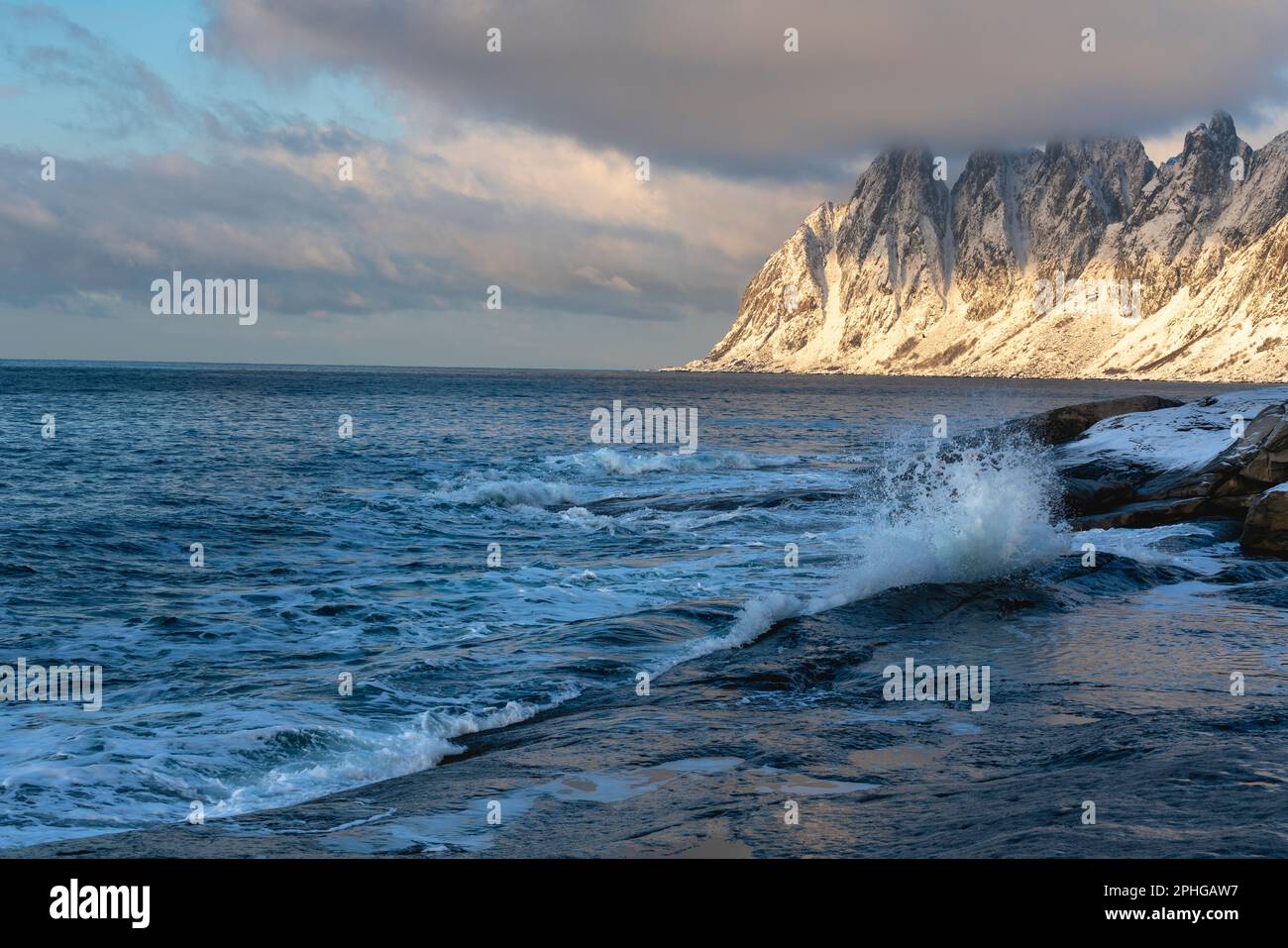 Am Fels sich brechende Wellen des Atlantik bei Tungeneset, Senja, Norwegen, mit den steilen Bergen Okshornan im Hintergrund. stürmisches Winterwetter Foto Stock