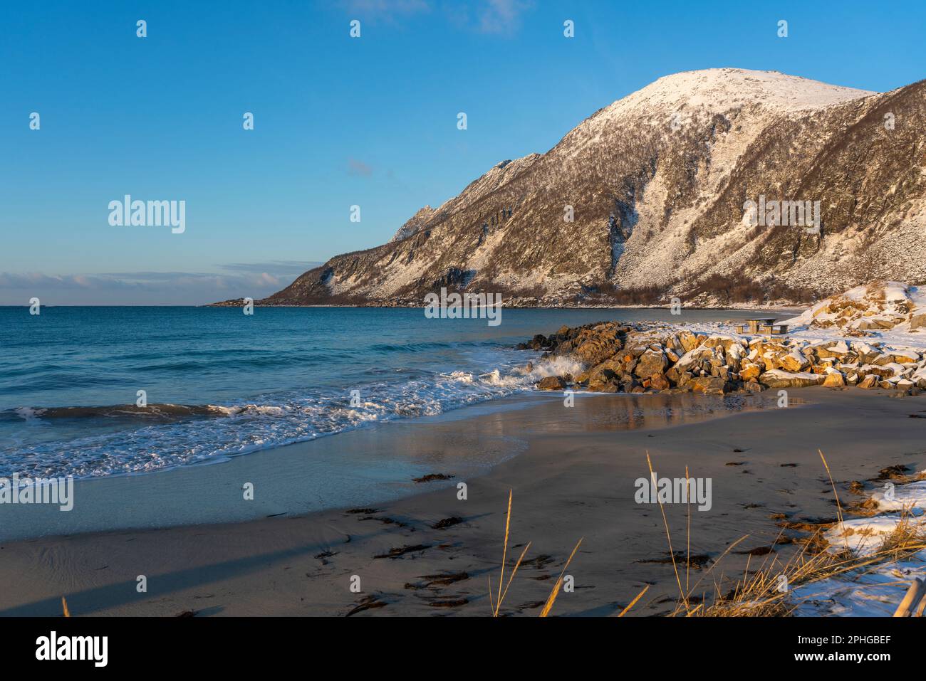 Vista panoramica sui fiordi e sulle ripide montagne innevate da Senja, Norvegia. Barca, pesci secchi, cespugli innevati e betulle sulla spiaggia. inverno Foto Stock