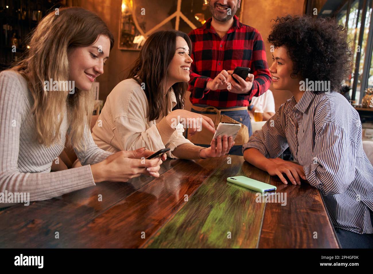 Le giovani ragazze del gruppo guardano il menu della caffetteria sui telefoni delle cellule per ordinare qualcosa da bere dal cameriere. Foto Stock
