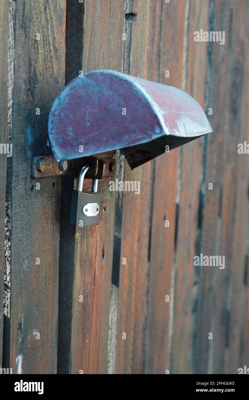 Lucchetto chiuso con coperchio in metallo che fissa il vecchio cancello di listelli in legno intemperiato Foto Stock