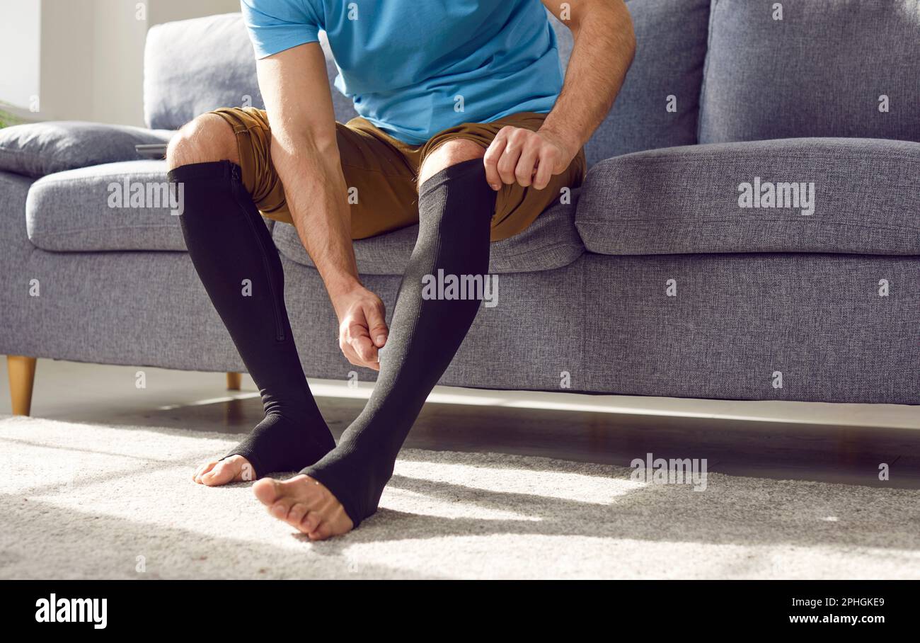 Uomo che mette su calze di compressione medica sulle gambe per la prevenzione delle vene varicose. Foto Stock