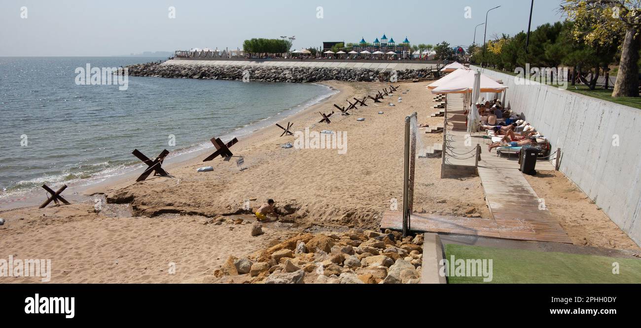 Odessa, Ucraina -2022: Barriere militari metalliche, ricci anticarro sulla spiaggia della città di mare. I vacanzieri si abbronzano accanto ai ricci anticarro in ferro. Recinzioni f Foto Stock