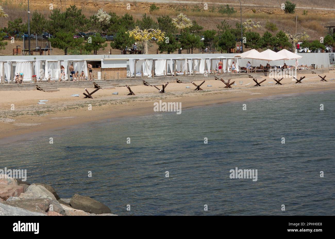 Odessa, Ucraina -2022: Barriere militari metalliche, ricci anticarro sulla spiaggia della città di mare. I vacanzieri si abbronzano accanto ai ricci anticarro in ferro. Recinzioni f Foto Stock