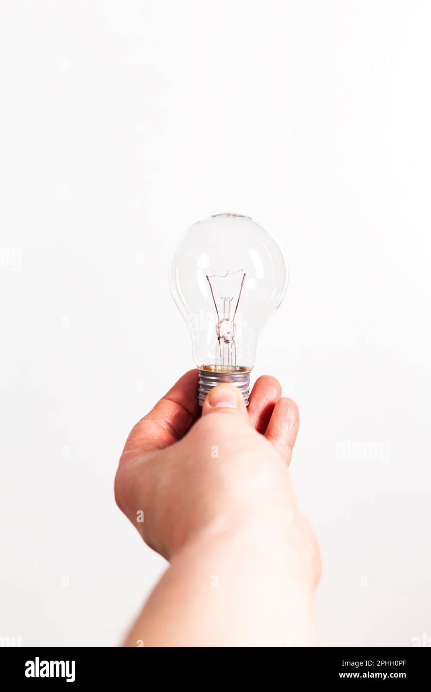 Primo piano di una mano umana che tiene una lampadina non illuminata su sfondo bianco. Foto Stock